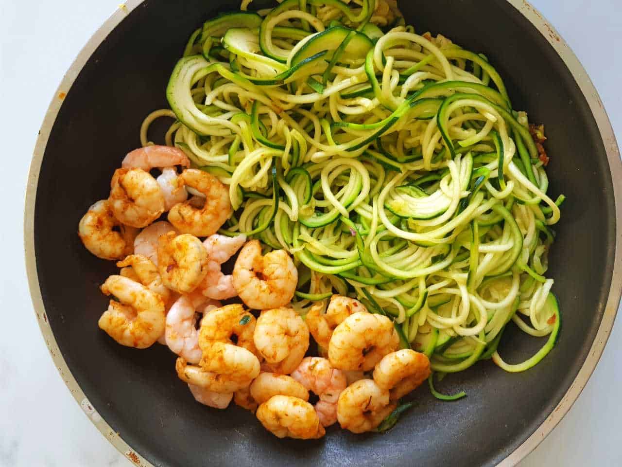 Zucchini noodles and shrimp in a pan on a marble table.