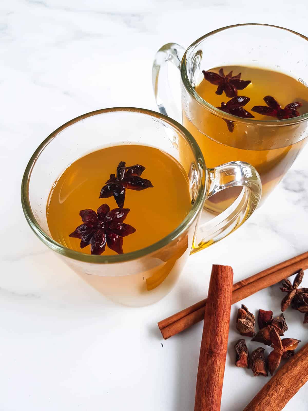 Glasses filled with star anise tea with cinnamon sticks on the side.