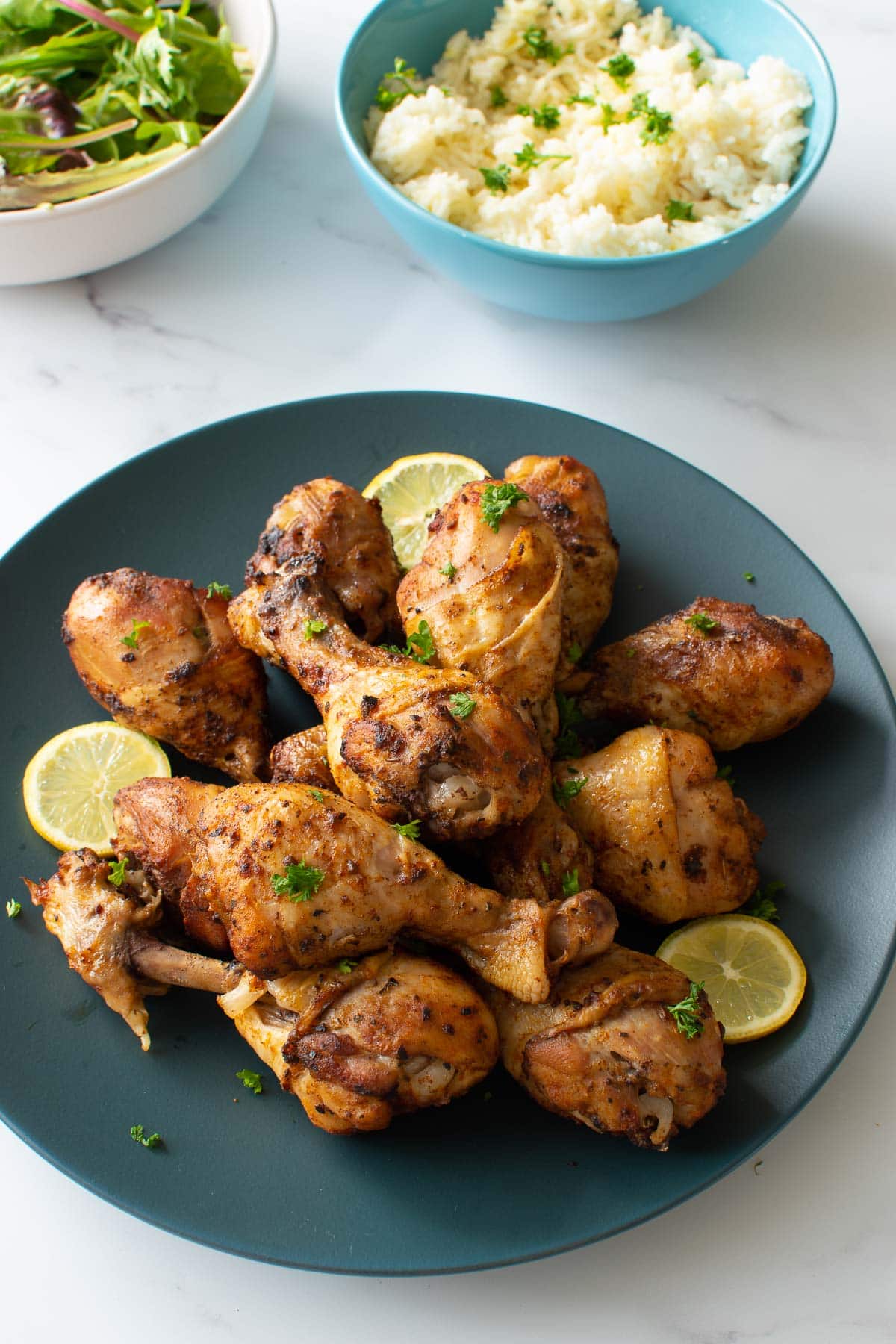 A plate of drumsticks, with salad and rice in the background.