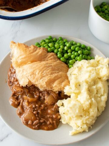 Minced beef puff pastry pie with peas and mashed potatoes.